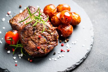 Barbekü yemeği. Siyah tahtada sebzeli et biftekleri ve otlar. Kapat..