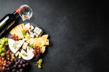 Peynir tabağı ve kırmızı şarap. Kesme tahtasındaki taze üzümlü el yapımı peynir seti. Siyah arkaplanda üst görünüm.