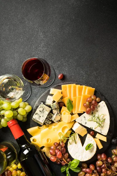 Cheese platter with craft cheese assortment on slate board and red wine at black background. Top view.
