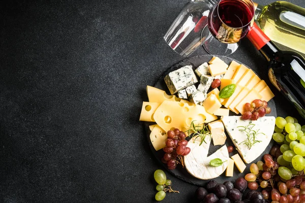 Cheese platter and red wine. Craft cheese set with grape on slate board. Top view at black background.
