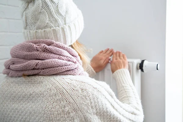 女性がバッテリーの近くで手を暖める 女性暖かく家の中で寒さを着た 暖房を節約 高価な公共料金 — ストック写真