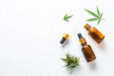 CBD yağı ve kenevir yaprakları beyaz masada. İlaç ve kozmetik ürünler. Düz görünüm.
