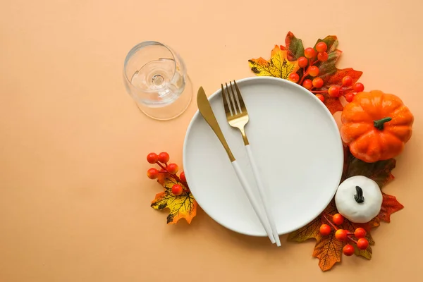 Fall table setting. White plate, golden cutlery and fall decorations at orange background. Flat lay image with copy space.