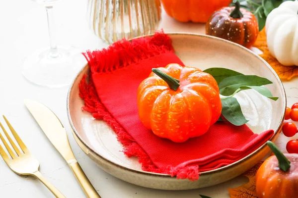 Fall table setting at white with decorations. Craft plate, golden cutlery, glass, candle and fall decorations.