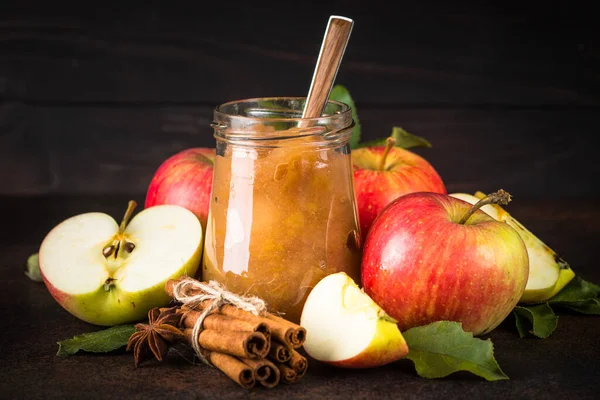 Apple jam with spices and fresh apples on dark stone background.