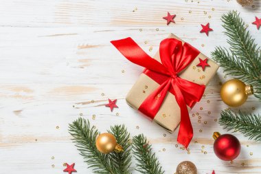 Kırmızı kurdeleli ve Noel süslemeli Noel hediyesi kutusu. Beyaz ahşap masadaki en üst manzara.