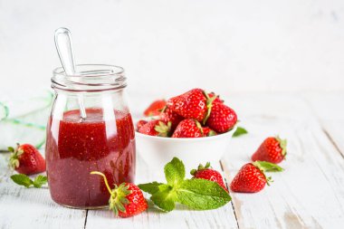 Beyaz masadaki cam kavanozda çilek reçeli.