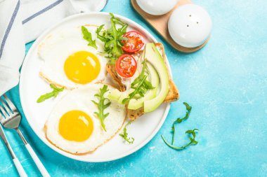 Kahvaltıda. Yağda yumurta, kızarmış ekmek, beyaz peynir, avokado ve taze salata. Sağlıklı yiyecekler. Mavi tabloda kopyalama alanı olan üst görünüm.