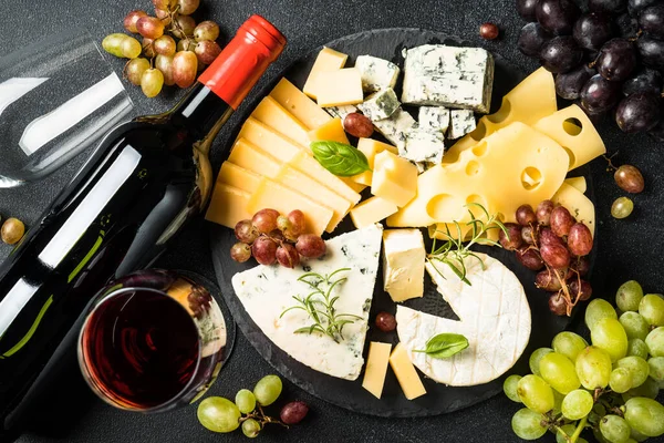 スレートボード上のクラフトチーズの品揃えと黒の背景に赤ワインのチーズプレッター トップビュー — ストック写真
