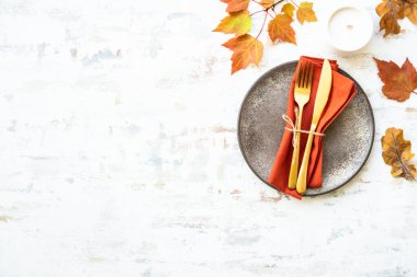 Sonbahar sofrası. Samimi sonbahar süslemeleri, el işi tabaklar ve beyaz arka planda altın çatal bıçak takımı..