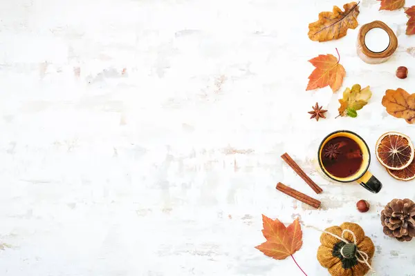 Fall background. Cozy autumn on white. Cup of spicy tea, autumn leaves, spices and decor. Flat lay with copy space.