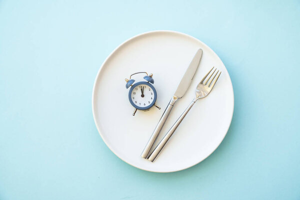 Intermittent fasting concept. Healthy eating, diet. White plate with cutlery and clock.