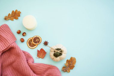 Sonbahar arkaplanı mavi. Sıcak örülü süveter, kuru yapraklar ve dekorasyonlar. Düz görünüm.