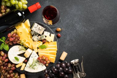 Peynir tabağı ve kırmızı şarap. Kaykay tahtasındaki üzümlü el yapımı peynir. Siyah arkaplanda üst görünüm.