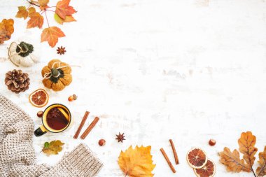Sonbahar arkaplanı. Bir fincan sıcak çay, sıcak kazak, sonbahar yaprakları, baharatlar ve beyaz süslemeler. Kopyalama alanı olan düz.