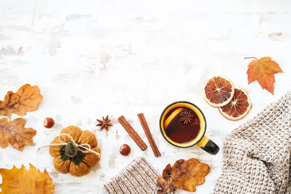 Cozy autumn background on white. Cup of spicy tea, warm sweater, autumn leaves, spices and decor. Flat lay with copy space.