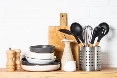 Kitchen table, kitchen utensils, plates, bowls, shakers and wooden cutting board, white modern interior. Modern kitchen interior.