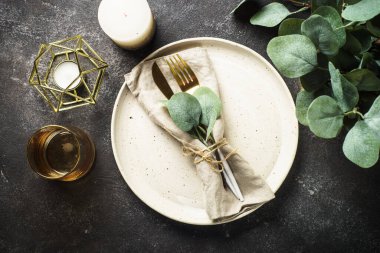 Table setting with white craft plate, cutlery and decorations at black stone table. Top view image.