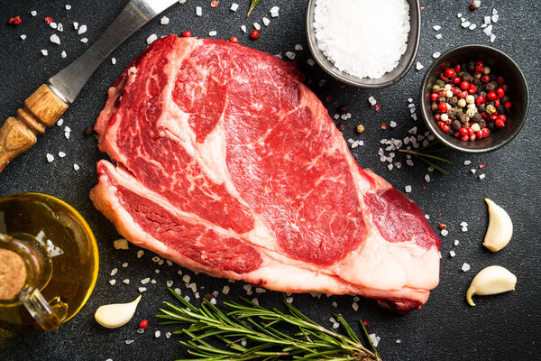 Beef steak with spices on black background. Ribeye steak raw meat. Top view with copy space.