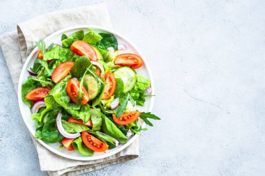 Yapraklı ve sebzeli yeşil salata. Vejetaryen yemeği, diyet yemeği. Taş masada kopyalama alanı olan üst görünüm.