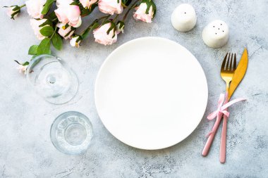 Masa seti beyaz tabak, çatal bıçak takımı ve gül çiçekli şarap kadehi. Yıldönümü ya da düğün için masa dekorasyonu. Kopyalama alanı olan düz.