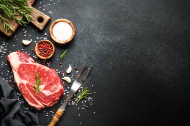 Biftek. Biftek pirzolası, baharat ve siyah arka planda bitkiler. Kopyalama alanı olan üst görünüm.