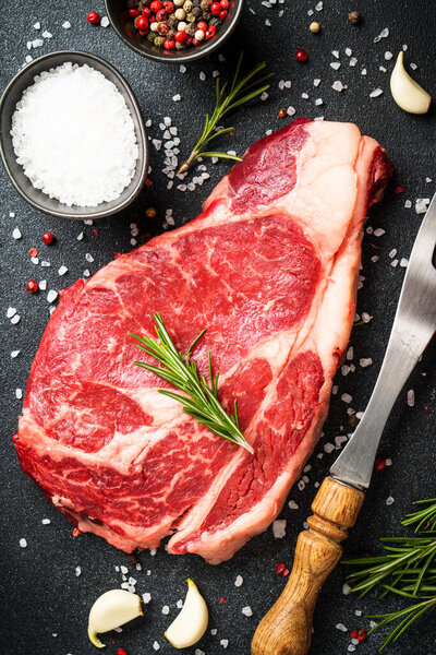 Beef steak with spices on black background. Ribeye steak raw meat. Top view with copy space.