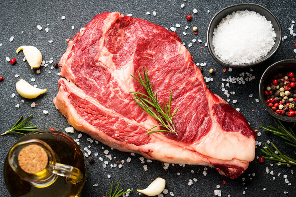 Beef steak with spices on black background. Ribeye steak raw meat. Top view.