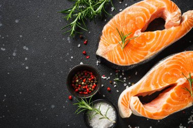 Siyah arkaplanda çiğ somon bifteği. Yemek pişirmek için malzemelerle üst görünüm.