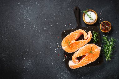 Siyah arkaplanda çiğ somon bifteği. Yemek pişirmek için malzemelerle üst görünüm.