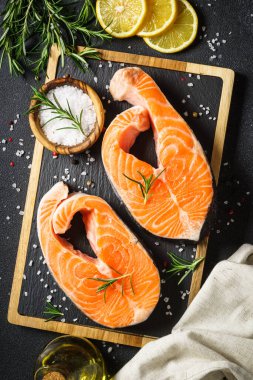 Taze balık. Siyah arka planda kesilmiş somon bifteği. Yemek pişirmek için malzemelerle üst görünüm.