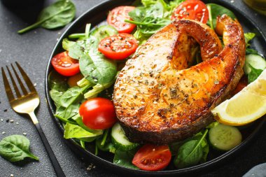 Somon bifteği ve siyah arka planda taze yeşil salata. Keto diyeti, sağlıklı yiyecekler.