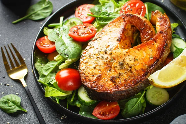 Somon bifteği ve siyah arka planda taze yeşil salata. Keto diyeti, sağlıklı yiyecekler.