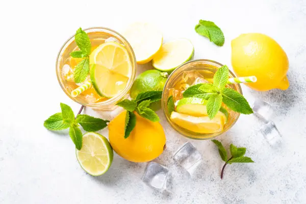 Iced tea. Black tea with lemon, lime, mint and ice. Cold lemonade, summer drink, white background. Top view with copy space.