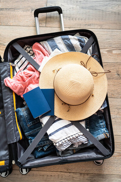 Open Suitcase with summer cloth, hat and passports. Travel concept. Flat lay image on wooden background.