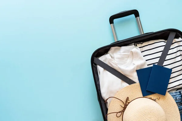 Open Suitcase with summer cloth, hat and passport on blue background. Flat lay image.