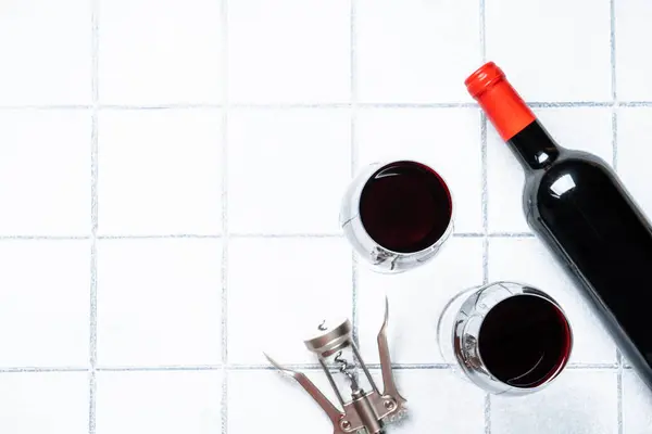 Red wine on white background. Two glases with wine, wine bottle and corkscrew with hard shadows.
