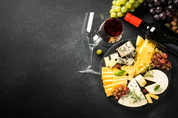 Cheese platter and red wine at black background. Cheese assortment on slate board. Top view.