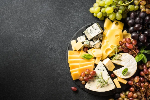 Cheese platter with craft cheese assortment and grape at black background. Top view with copy space.