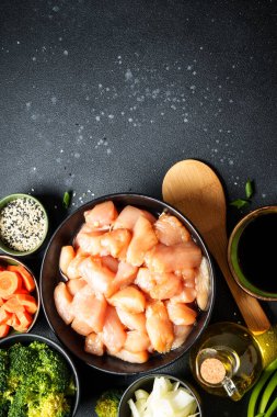 Asya yemekleri hazırlığı. Soya soslu tavuk, kırmızı biber, brokoli ve siyah arka planda soğan. Çiğ yemek, yemek tarifi malzemeleri. Dikey.