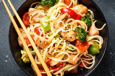 Siyah kasede tavuk ve sebzeli Asya eriştesi. Üst görünüm kapat.