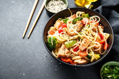 Kızarmış tavuğu sebzeyle karıştır ve siyah arka planda erişte. Asya mutfağı. Kapat..