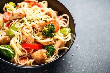 Kızarmış tavuğu sebzeyle karıştır ve siyah arka planda erişte. Asya mutfağı. Kapat..