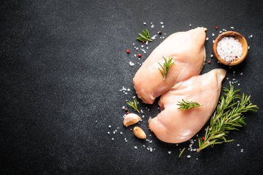 Tavuk eti. Çiğ tavuk göğsü ve siyah arka planda baharatlar. Üst görünüm.