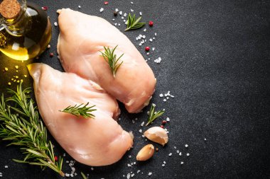 Tavuk eti. Çiğ tavuk göğsü ve siyah masada baharatlar. Üst görünüm.