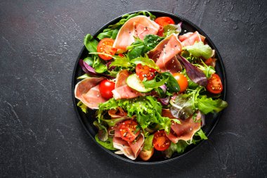 Siyah arka planda yeşil salata. Jamonlu taze salata, yeşil salata yaprakları ve domates. Metin için boşluk olan üst görünüm.