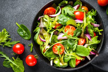 Arka planda siyah kasede salata. Sağlıklı yeşil sebze salatası, diyet menüsü. Üst görünüm.