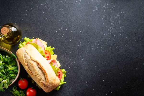 加生菜 西红柿和火腿的查巴塔三明治 放在有烹调配料的黑餐桌上 带有文本空间的顶部视图 — 图库照片