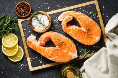 Taze balık. Siyah arka planda kesilmiş somon bifteği. Yemek pişirmek için malzemelerle üst görünüm.