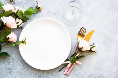 Masa seti beyaz tabak, çatal bıçak takımı ve gül çiçekli şarap kadehi. Yıldönümü ya da düğün için masa dekorasyonu. Kopyalama alanı olan düz.